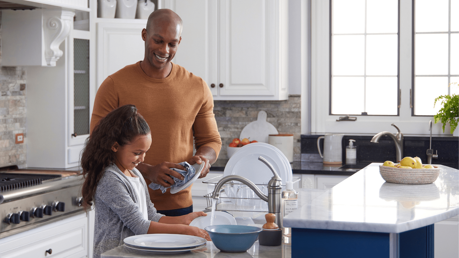 Father and daughter washing dishes at kitchen sink